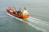 A large container ship laden with containers leaves a wide wake as it heads in to port