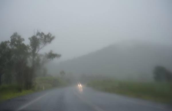a blurry view of a road through a car windscreen with headlights of an approcaing car in the distance