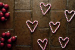 Christmas candy background pattern with red and white striped candy canes arranged as heart shapes on brown tiles with red Christmas baubles, overhead view