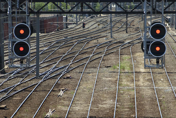 Two red railway signals on overhead gantries suspended over multiple criss crossing tracks