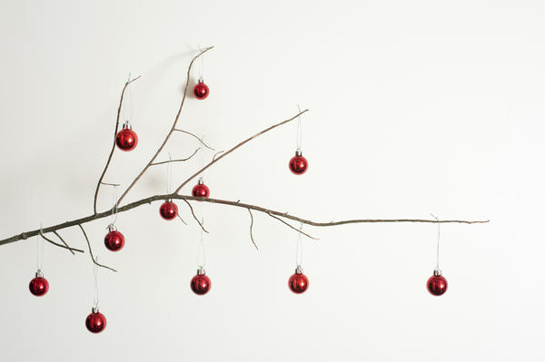 Modern decorated twig Christmas tree with a dried leafless branch decorated with colorful red baubles to celebrate the holiday, over white