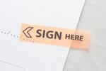 a sticky marker on a contract document highlighting where the sign and date