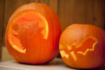 Two glowing Halloween pumpkin jack-o-lanterns with handmade decoration of a bat and howling wolf or werewolf